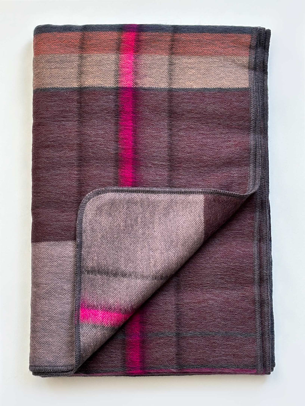 A folded plaid blanket with a color-blocked pattern in shades of brown, burgundy, and gray, featuring bright magenta pink stripes, shown on a plain white background.