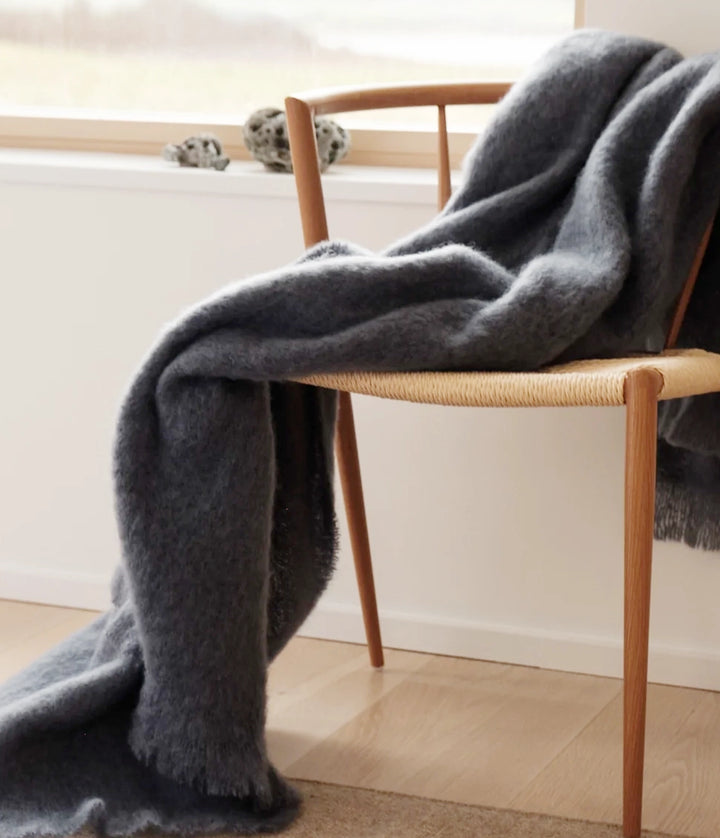 Navy mohair blanket draped over a wooden chair in a minimalistic room.